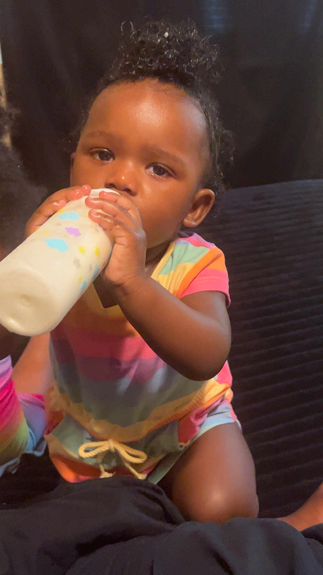 Ayla is registered to the contest to win money with this photo: toddler, child, baby, drinking, milk_bottle, colorful_clothing, striped_outfit, curly_hair, indoors, sitting, person, face, hand, milk, cute, young_child, portrait, infant, skin, expression