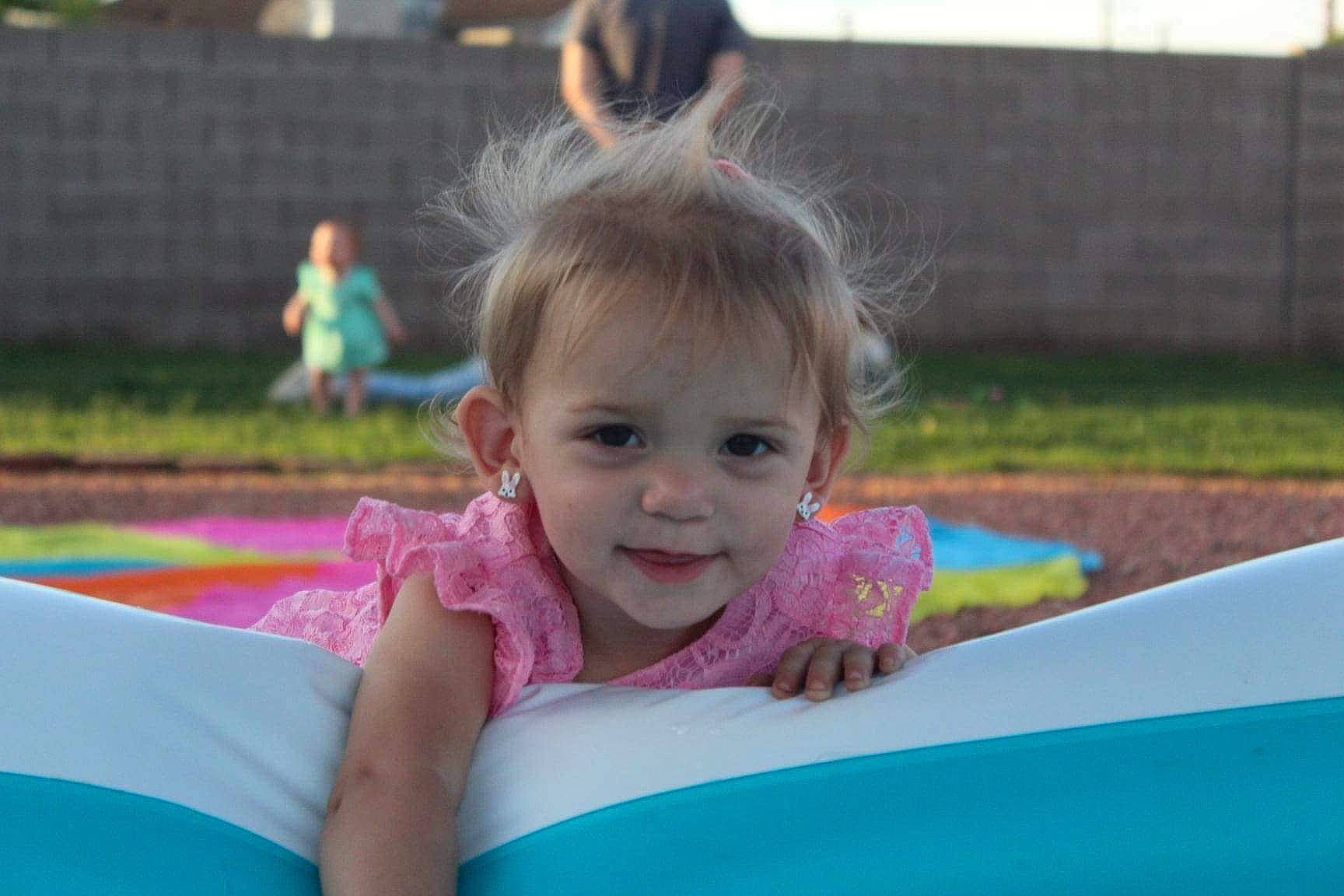 Jacklyn is registered to the contest to win money with this photo: baby, baby_toddler_clothing, child, city, event, face, fun, grass, happy, joy, leisure, magenta, outdoor_play_equipment, person, pink, plant, play, recreation, sitting, smile