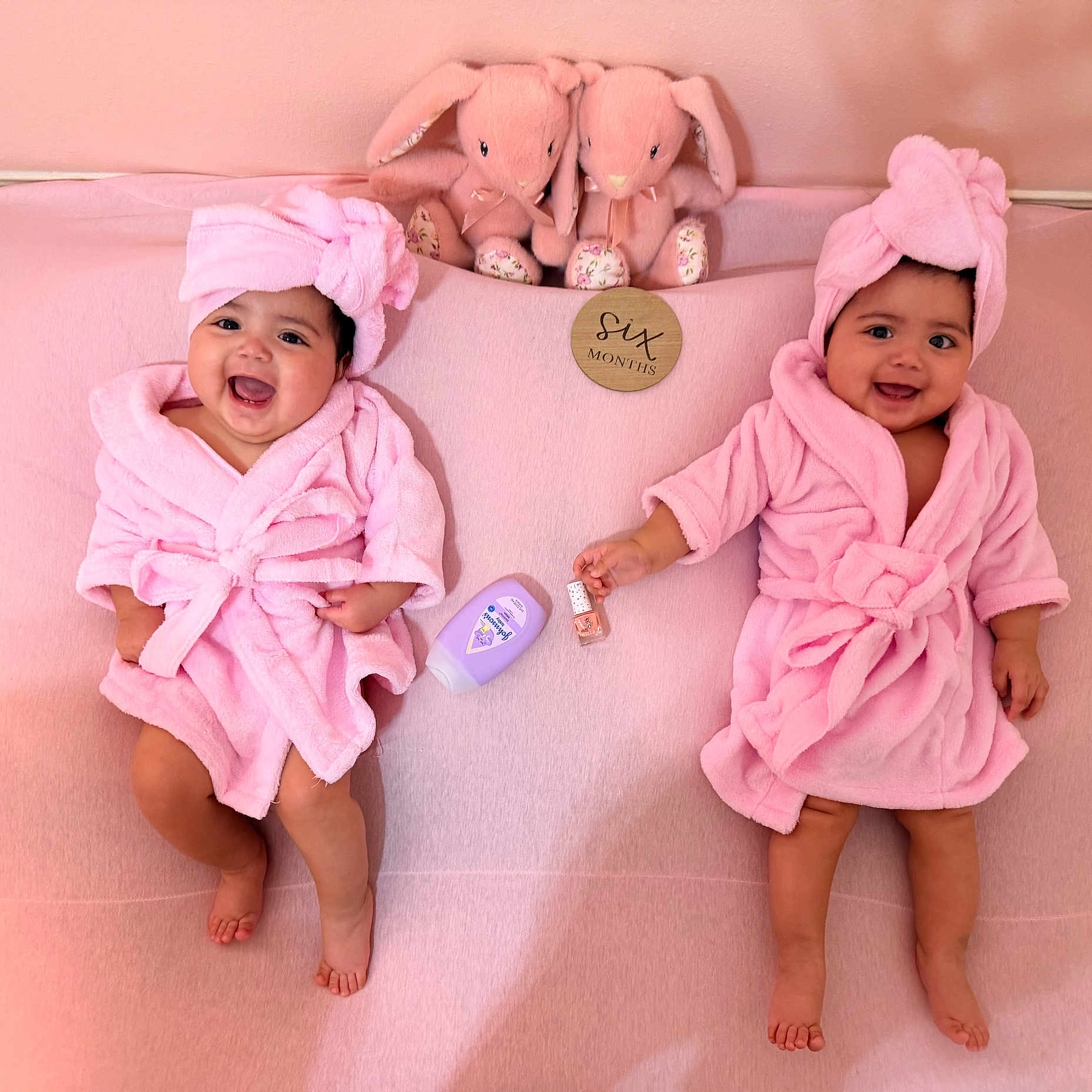 Joanna And Elianna is registered to the contest to win money with this photo: babies, twins, infants, smiling, pink, bathrobes, towels, turbans, bunny_toys, nursery, milestone, six_months, portrait, indoor, lying_down, baby_care, blanket, happy, siblings, photography