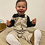 baby, child, smiling, corduroy, overalls, shoes, blanket, indoors, happy, cute, person, portrait, sitting, clothing, footwear, face, head, infant, soft_texture, minimalist