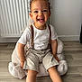 Ayden a rejoint le concours — aidez-le/la à gagner de superbes lots ! casual_clothing, child, curly_hair, cute, flooring, happy, home, indoor, light_skin, person, plush_chair, portrait, radiator, seated, shorts, smiling, suspenders, toddler, white_shirt, young_child