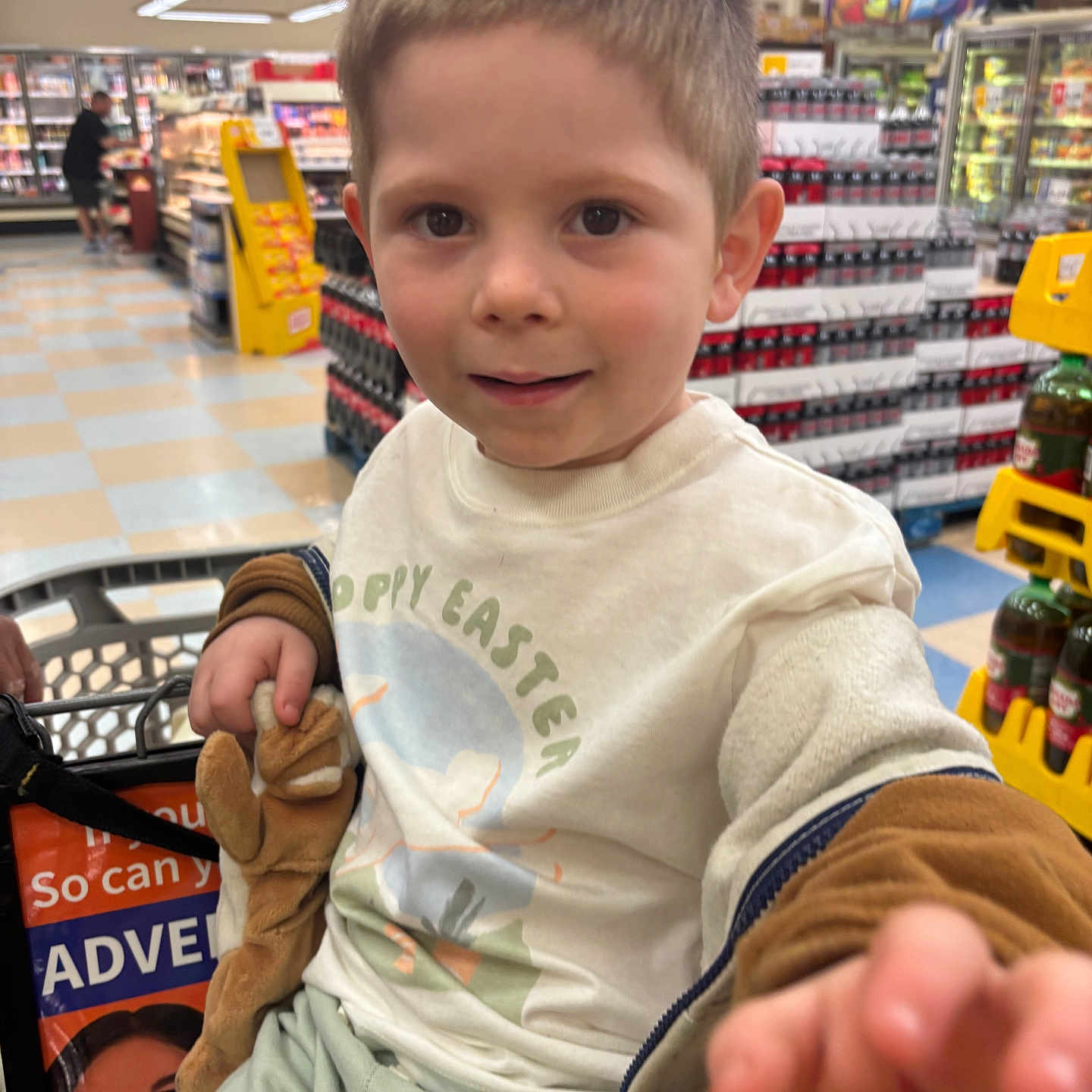 Jaxson is registered to the contest to win money with this photo: child, shopping_cart, grocery_store, toy, stuffed_animal, clothing, face, person, indoor, supermarket, shelf, bottle, drink, product, floor, tile, hand, shorts, expression, casual