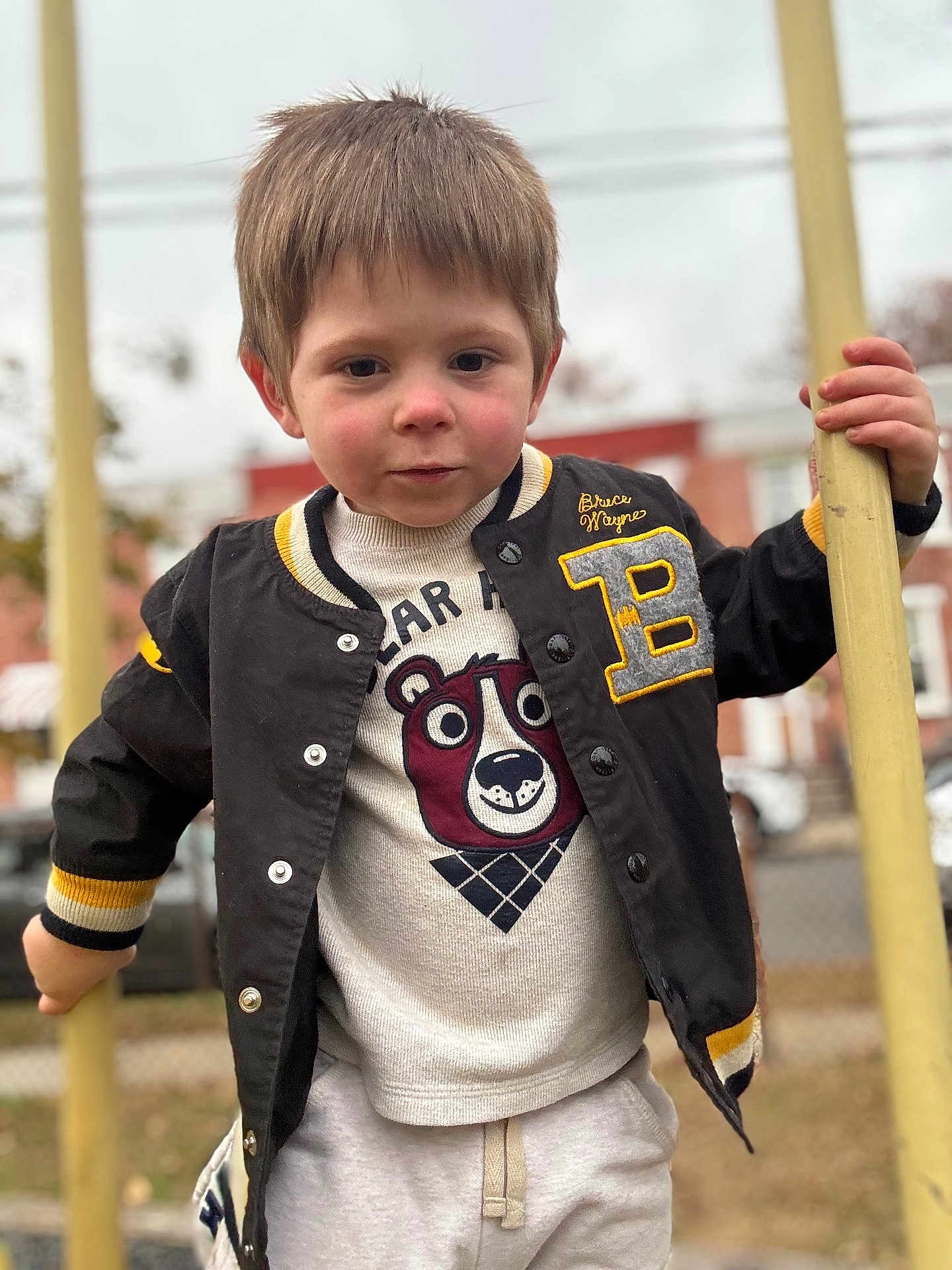 Jaxson joined the competition — help win amazing prizes! child, boy, jacket, sweater, bear_graphic, outdoor, playground, yellow_bars, clothing, face, person, casual_wear, expression, daylight, young, portrait, holding, hands, background_blur, urban