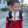 Jaxson is registered to the contest to win money with this photo: child, boy, smiling, portrait, outdoor, sidewalk, street, neighborhood, spiderman, superhero, jacket, backpack, clothing, house, urban, cars, roses, no_parking_sign, daylight, photography