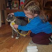 Elsa joined the competition — help win amazing prizes! blue_sweatshirt, braided_hair, brown_couch, carpet, cat, child, curtains, flooring, household_items, imaginative_play, indoor, maroon_pants, pet, playing, shelves, sitting, stethoscope, tabby_cat, toy, wooden_floor