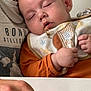 adult, baby, bib, casual, chain, child, closeup, clothing, comfort, face, gentle, hand, indoor, orange, peaceful, rest, skin, sleeping, table, white