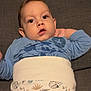 baby, blue_shirt, casual, child, comfortable, couch, curious, face, gray_couch, hand_behind_head, home, indoors, infant, mickey_mouse, pants, patterned_clothing, person, relaxed, wide_eyes, young_child