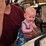 baby, adult, restaurant, table, phone, blue_dress, maroon_shirt, eating, holding, smiling, indoor, people, furniture, chair, hand, face, food, casual, happy, seated