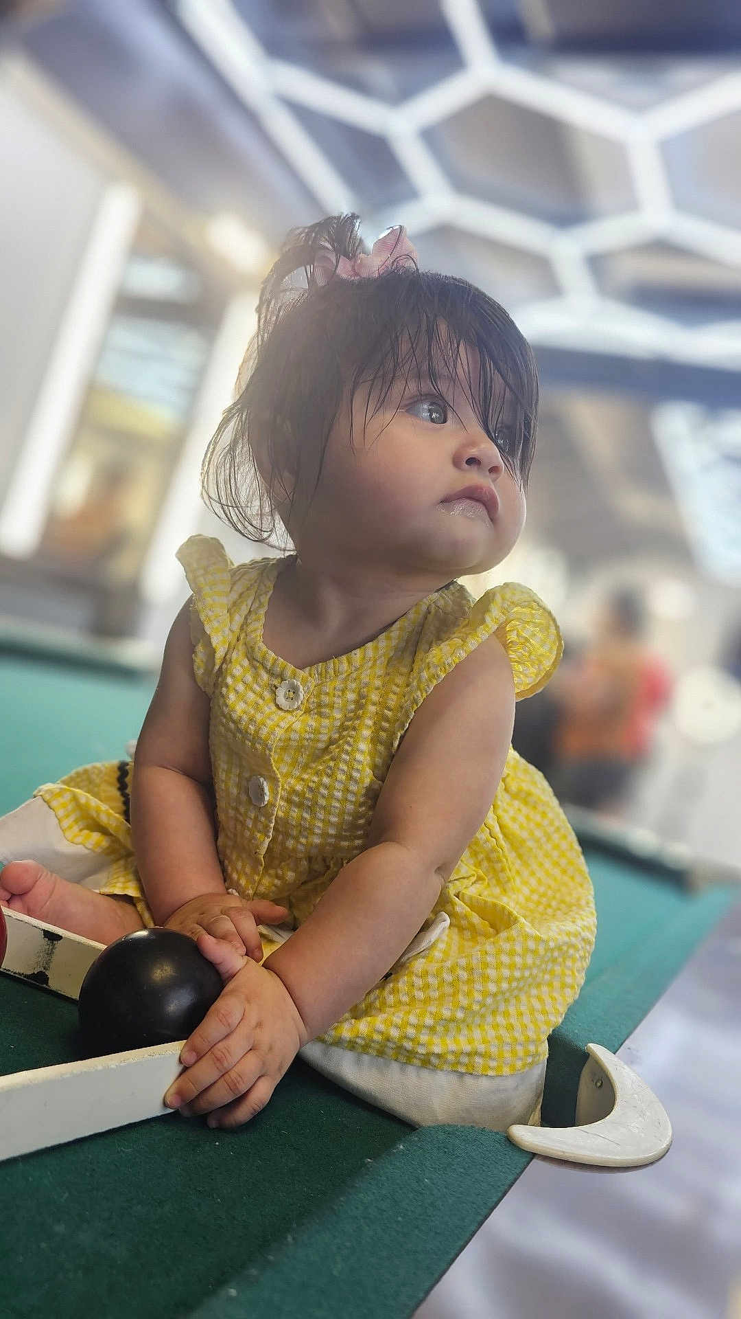 Elizabeth joined the competition — help win amazing prizes! toddler, child, yellow_dress, pool_table, billiard_ball, indoor, curly_hair, sitting, playing, soft_lighting, modern_ceiling, hand, face, portrait, casual, cute, young_child, curious, closeup, daylight