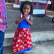 Maëllys a rejoint le concours — aidez-le/la à gagner de superbes lots ! child, girl, boy, traditional_dress, barefoot, curly_hair, smiling, outdoor, concrete, colorful, festival, cultural_event, pillar, purple_fence, casual_clothing, people, portrait, happy, daylight, hands_together