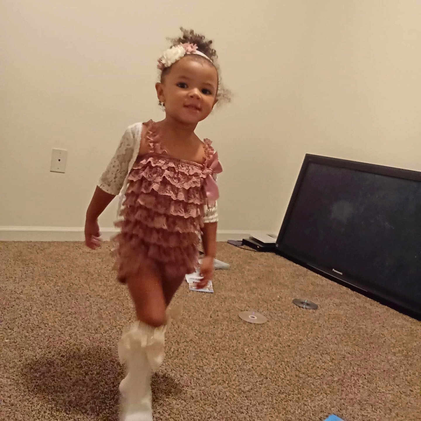 E Zaylee is registered to the contest to win money with this photo: boot, carpet, child, dvd_case, dvd_disc, flower_headband, girl, hair, head, household_items, indoor, living_room, motion_blur, playful, ruffled_dress, smile, television, toddler, walking, wall_outlet