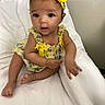 baby, bed, big_eyes, blanket, bow, child, curly_hair, cute, fabric, hands, headband, indoor, infant, portrait, sitting, skin, smile, toes, wall, yellow_dress