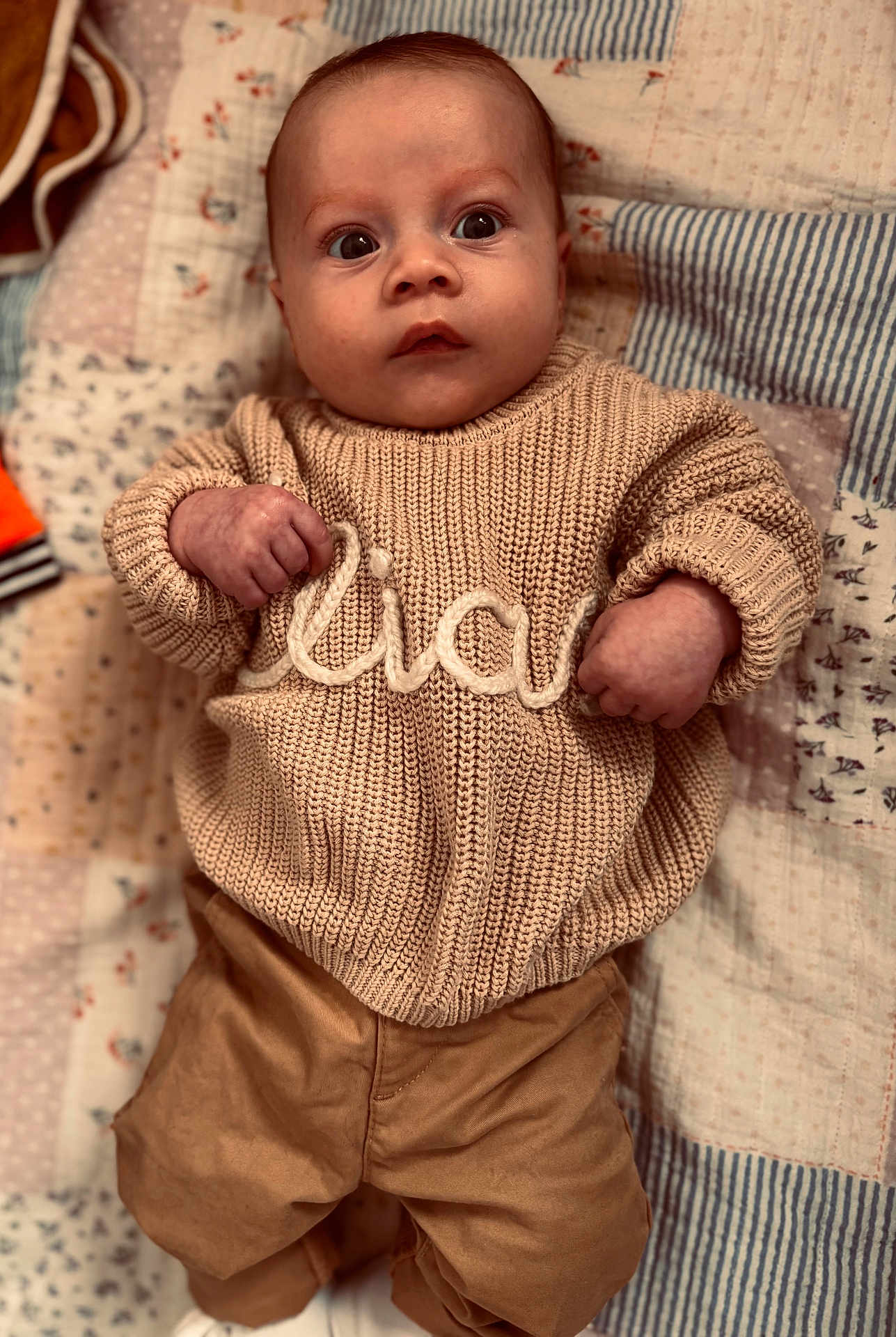 élias participe au concours pour gagner de l'argent avec cette photo : baby, infant, face, wide_eyes, sweater, knitwear, patchwork_quilt, blanket, pants, clothing, portrait, lying_down, hands, fists, rosy_cheeks, soft_lighting, cute, indoor, bedding, newborn