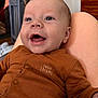 baby, infant, newborn, smiling, face, eyes, mouth_open, onesie, clothing, text_on_clothing, lap, skin, close_up, portrait, nursery, crib, dresser, furniture, happy, button