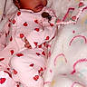 baby, sleeping, pink_onesie, ladybug_pattern, blanket, rainbow_pattern, pacifier_clip, strawberry, slipper, infant, cute, soft_texture, resting, child, cozy, indoor, newborn, person, toddler, comfort