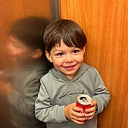 Imrân participe au concours pour gagner de l'argent avec cette photo : child, boy, smiling, soda_can, reflection, hoodie, short_hair, indoor, wood_panel, leather_surface, happy, casual_clothing, portrait, young, cute, holding_object, person, face, standing, bright