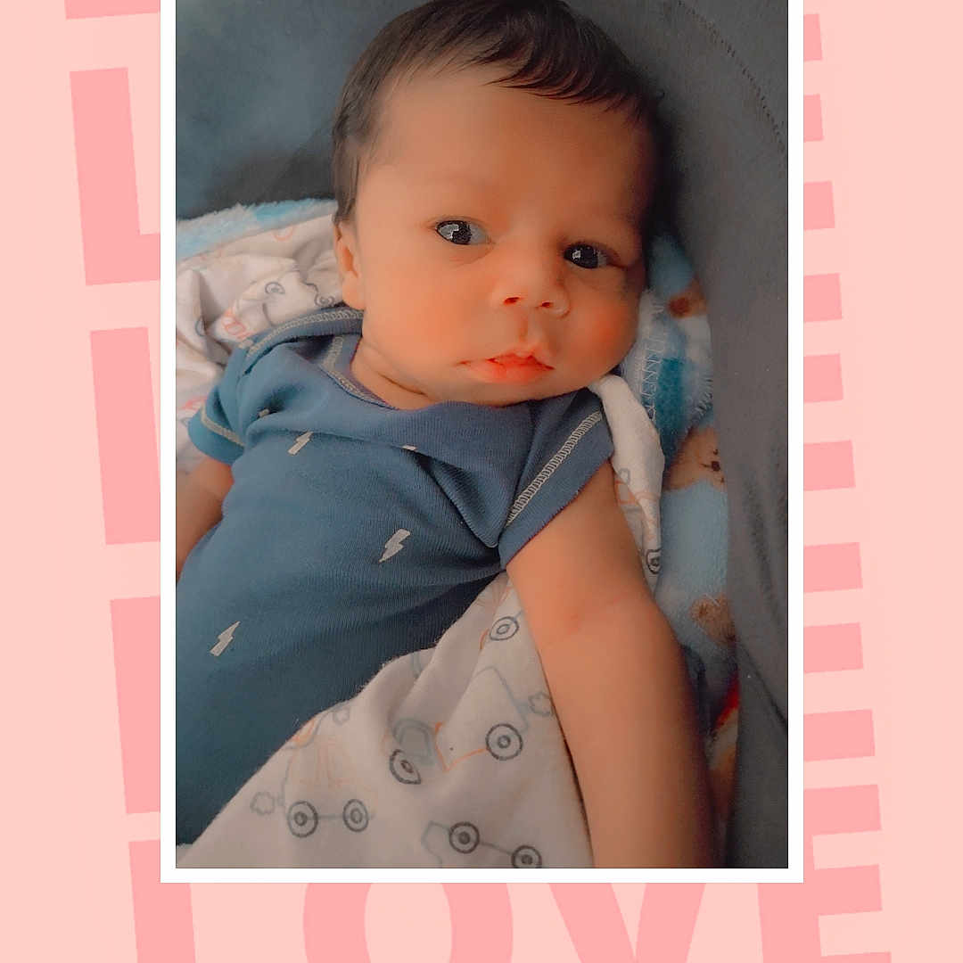 Ny'Sir is registered to the contest to win money with this photo: baby, baby_bed, blanket, blue_clothing, child, close_up, crib, cute, eyes, face, indoor, infant, looking_at_camera, love_text, lying_down, photo_frame, photography, pink_background, portrait, sitting