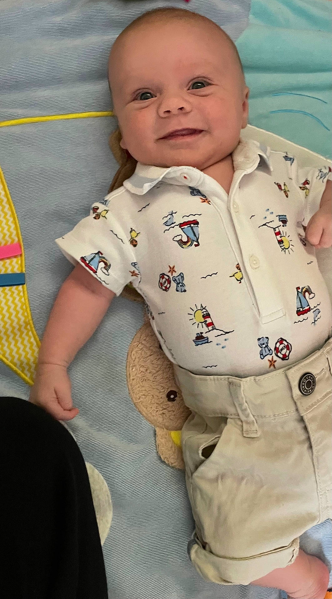 George joined the competition — help win amazing prizes! baby, blanket, child, clothing, comfort, cute, face, happy, indoor, infant, lying_down, patterned_shirt, person, plush_toy, shirt, shorts, skin, small_child, smiling, young_child
