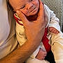George is registered to the contest to win money with this photo: baby, blanket, closeup, comfort, couch, cozy, expression, face, hand, holding, indoor, infant, newborn, pajamas, person, portrait, red_clothing, resting, skin, white_clothing