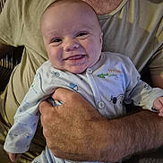 George is registered to the contest to win money with this photo: adult, arm, baby, closeup, clothing, comfortable, couch, expression, face, hand, happy, head, holding, indoor, pajamas, person, seated, skin, smile, tongue