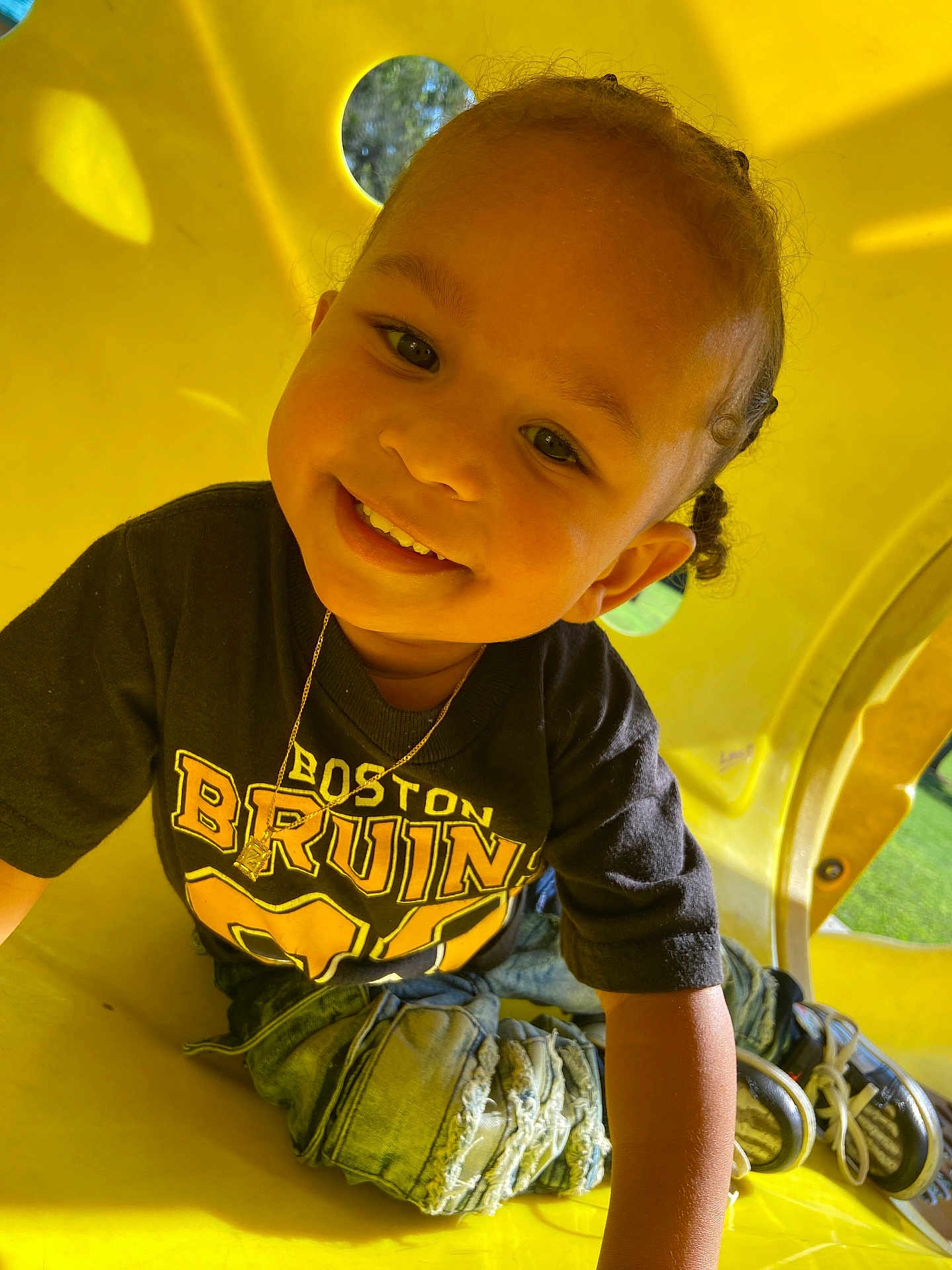Zaelyn is registered to the contest to win money with this photo: child, toddler, smiling, braided_hair, black_tshirt, boston_bruins, jeans, ripped_jeans, sneakers, playground, yellow_tunnel, outdoor, sunlight, happy, cute, portrait, casual_clothing, play, young_child, person