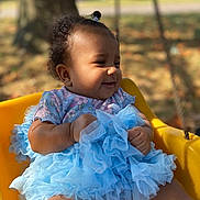Lehlani joined the competition — help win amazing prizes! baby, child, smiling, blue_tutu, yellow_chair, outdoor, sunlight, curly_hair, happy, floral_outfit, infant, cute, portrait, nature, autumn, trees, blurred_background, sitting, toddler, playful
