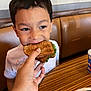 child, boy, sandwich, hand, restaurant, booth_seating, table, fries, cup, food, casual_dining, eating, smiling, indoor, clothing, white_shirt, lettuce, bread, person, happy