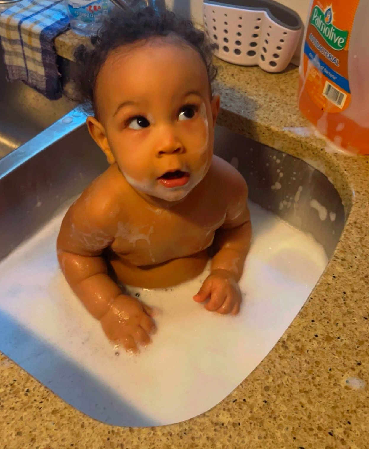Torion is registered to the contest to win money with this photo: baby, bath, child, cleaning, container, curious, curly_hair, domestic, expression, face, foam, hands, household, infant, kitchen_counter, liquid, sink, skin, soap_bubbles, water