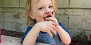Paxton joined the competition — help win amazing prizes! blue_clothing, child, concrete_wall, face, food, ground, hair, hands, happy, light, messy, outdoor, overalls, seat, shadow, smiling, snack, table, toddler, umbrella