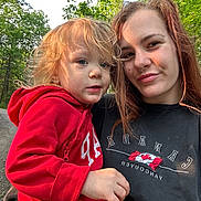 Paxton is registered to the contest to win money with this photo: car, casual, child, daylight, forest, gravel, greenery, holding, hoodie, nature, outdoor, person, portrait, red_clothing, road, selfie, smile, toddler, trees, woman
