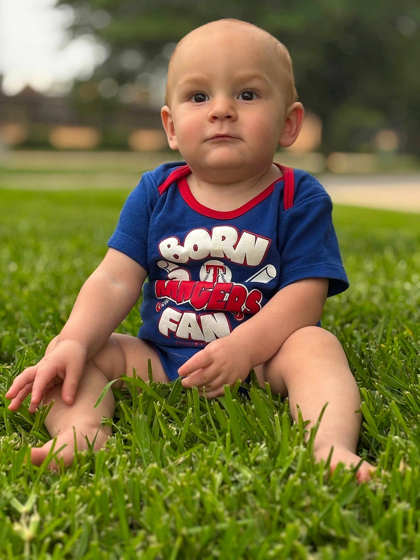 Garret is registered to the contest to win money with this photo: baby, child, grass, outdoor, blue_clothing, onesie, sitting, serious_expression, barefoot, summer, portrait, nature, infant, cute, young, person, greenery, daylight, casual, park