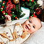 baby, infant, smiling, reindeer_onesie, christmas_tree, holiday_decor, nutcracker, red_ornaments, green_ornaments, white_cushion, festive, cute, child, portrait, indoors, happy, seasonal, celebration, decorations, closeup