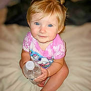 Lenox is registered to the contest to win money with this photo: baby, bed, blonde_hair, blue_eyes, child, close_up, cute, holding_object, indoor, innocence, person, pink_shirt, portrait, sitting, smiling, soft_lighting, tie_dye, toddler, water_bottle, young_child