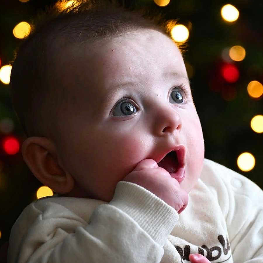 Seven participe au concours pour gagner de l'argent avec cette photo : baby, bokeh, child, closeup, clothing, curious, cute, expression, face, festive, fingers, hand, holiday, indoors, infant, lights, portrait, soft_light, white_sweater, young
