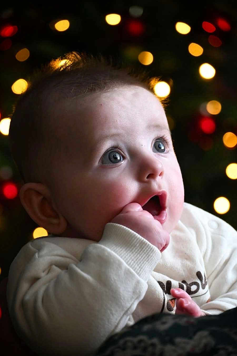 Seven participe au concours pour gagner de l'argent avec cette photo : baby, child, face, expression, curious, hand, fingers, clothing, white_sweater, portrait, closeup, indoors, lights, bokeh, holiday, festive, cute, infant, young, soft_light