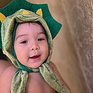 Alessandro is registered to the contest to win money with this photo: baby, child, dinosaur_hat, green_hat, smiling, cute, portrait, face, headwear, infant, soft_texture, closeup, indoors, happy, adorable, costume, babywear, skin, expression, young