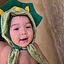 baby, child, dinosaur_hat, green_hat, smiling, cute, portrait, face, headwear, infant, soft_texture, closeup, indoors, happy, adorable, costume, babywear, skin, expression, young