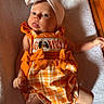 Eliana is registered to the contest to win money with this photo: baby, child, headband, bow, orange_clothing, romper, plaid, blanket, floor, wooden_floor, indoor, cute, infant, person, lying_down, expression, tongue_out, texture, soft, casual