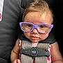 baby, child, glasses, car_seat, harness, purple_glasses, infant, cute, face, hand, clothing, safety, seatbelt, straps, curly_hair, indoor, person, portrait, closeup, expression