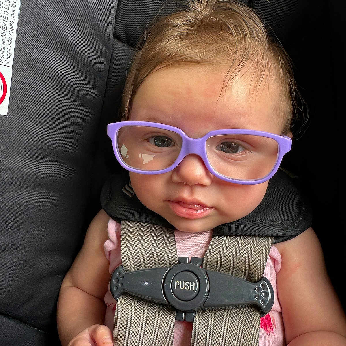 Kennedie joined the competition — help win amazing prizes! baby, car_seat, child, closeup, clothing, curly_hair, cute, expression, face, glasses, hand, harness, indoor, infant, person, portrait, purple_glasses, safety, seatbelt, straps