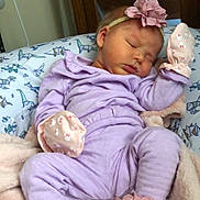 Araya Hope is registered to the contest to win money with this photo: baby, sleeping, infant, lavender_outfit, mittens, booties, flower_headband, blanket, pillow, dinosaur_pattern, soft_texture, indoors, peaceful, cute, child, newborn, resting, cozy, pink, purple