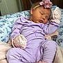 baby, sleeping, infant, lavender_outfit, mittens, booties, flower_headband, blanket, pillow, dinosaur_pattern, soft_texture, indoors, peaceful, cute, child, newborn, resting, cozy, pink, purple