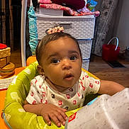 Ariana is registered to the contest to win money with this photo: baby, child, onesie, baby_walker, cup, indoor, floor, toy, face, hand, expression, curious, clothing, infant, furniture, home, person, sitting, wooden_floor, decor