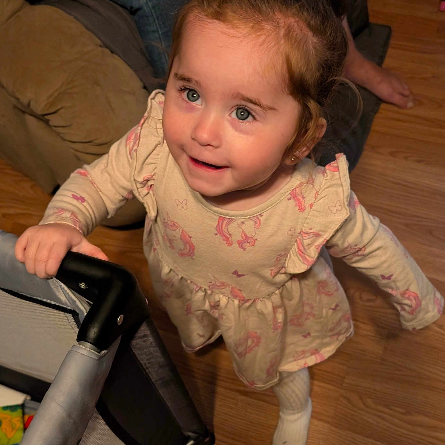 Elianna is registered to the contest to win money with this photo: child, clothing, cozy, dress, face, floor, foot, furniture, hair, happy, indoor, light, long_sleeve, person, playful, smiling, sock, stroller, toddler, wooden_floor