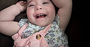 Elianna is registered to the contest to win money with this photo: arms_up, baby, child, clothing, cute, face, floral_top, hair, happy, indoors, infant, person, pink_overalls, portrait, relaxing, skin, sleeveless, smiling, teeth, toddler