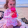 Elianna joined the competition — help win amazing prizes! bag, beach, cherry_pattern, child, curious, hair, ocean, outdoor, pink, portrait, quilt, sand, sandals, sippy_cup, sitting, sky, sunny, swimsuit, toddler, waves