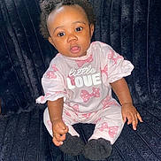 Omiyah joined the competition — help win amazing prizes! baby, child, infant, pink_clothing, bows, sitting, couch, plush, curly_hair, face, expression, cute, indoors, portrait, person, black_hair, black_socks, soft_fabric, comfortable, young