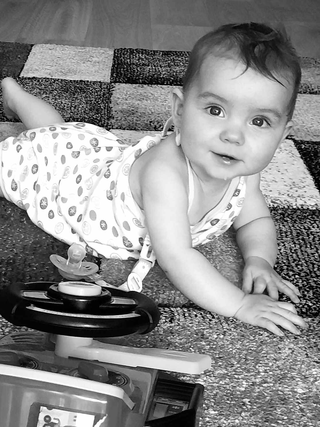 ïvi a rejoint le concours — aidez-le/la à gagner de superbes lots ! baby, black_and_white, carpet, child, clothing, cute, expression, eyes, face, floor, hand, indoor, infant, pattern, person, play, smiling, steering_wheel, toddler, toy