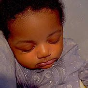 Milani is registered to the contest to win money with this photo: baby, sleeping, infant, onesie, purple_clothing, curly_hair, blanket, closeup, peaceful, cute, child, indoors, face, head, resting, cozy, portrait, soft_lighting, warm_colors, toddler