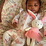baby, child, plush_toy, bunny, blanket, pajamas, floral_pattern, sleepwear, soft_toy, cute, infant, lying_down, indoors, comfort, pink, white, cozy, portrait, young_child, nursery